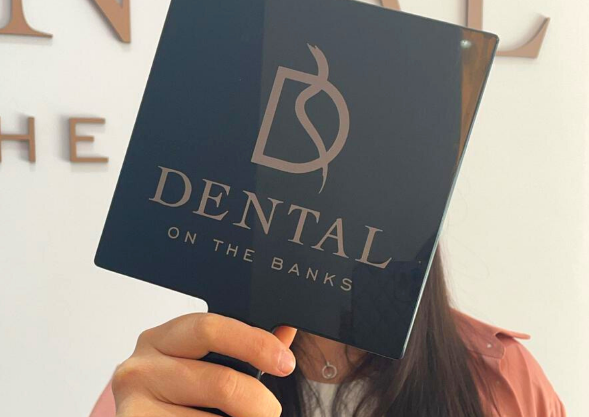 5 signs of healthy teeth woman holding up hand mirror at dental on the banks